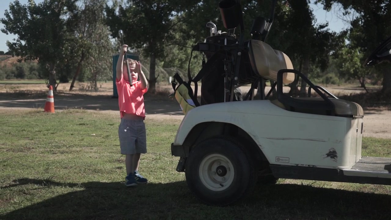 Un bambino piccolo prende una mazza da golf dal retro di un golf cart