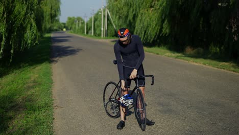 sportsman putting on his helmet on a bicycle, full length