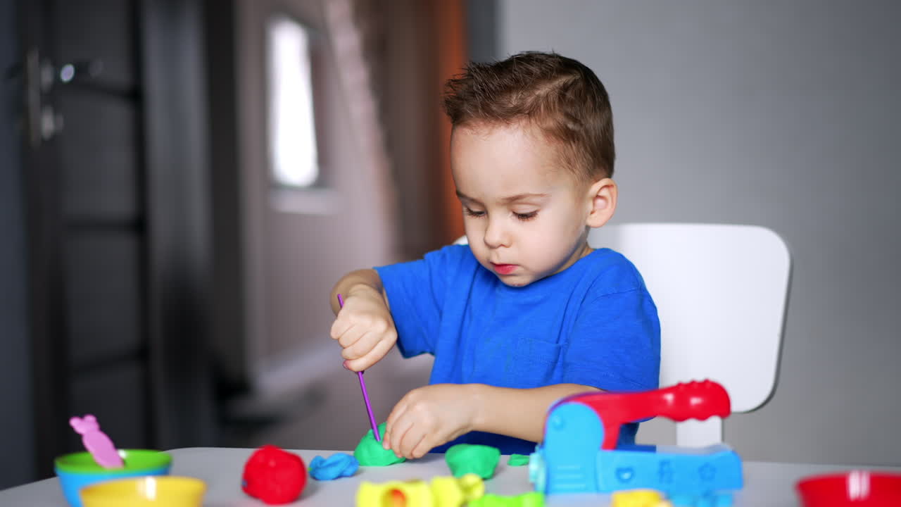 Cute two year old boy is focused on the game with plasticine. Busy kid uses a stick to cut the piece.