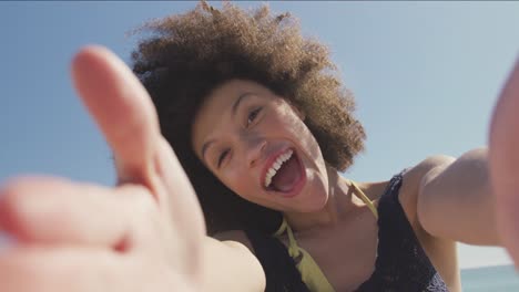 Mixed-race-woman-sending-kisses-through-camera-at-beach-