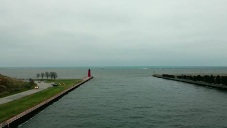 Aerial-shot-over-a-river-on-a-cloudy-day,-a-red-lighthouse-in-the-background