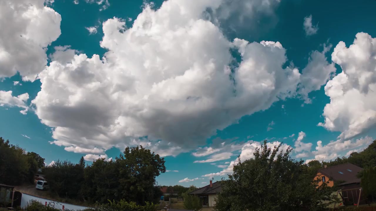 Time-lapse di nuvole che scorrono su un cielo turchese sopra un sobborgo con alberi e case