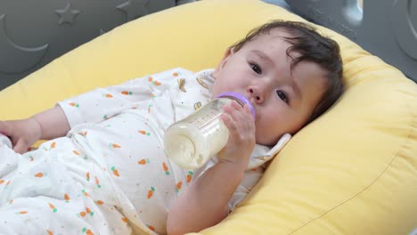 Linda-Niña-De-Un-Año-Bebiendo-Una-Botella-De-Leche-Mientras-Está-Acostada-Sobre-Una-Almohada-Amarilla---Primer-Plano,-Tiro-Estático