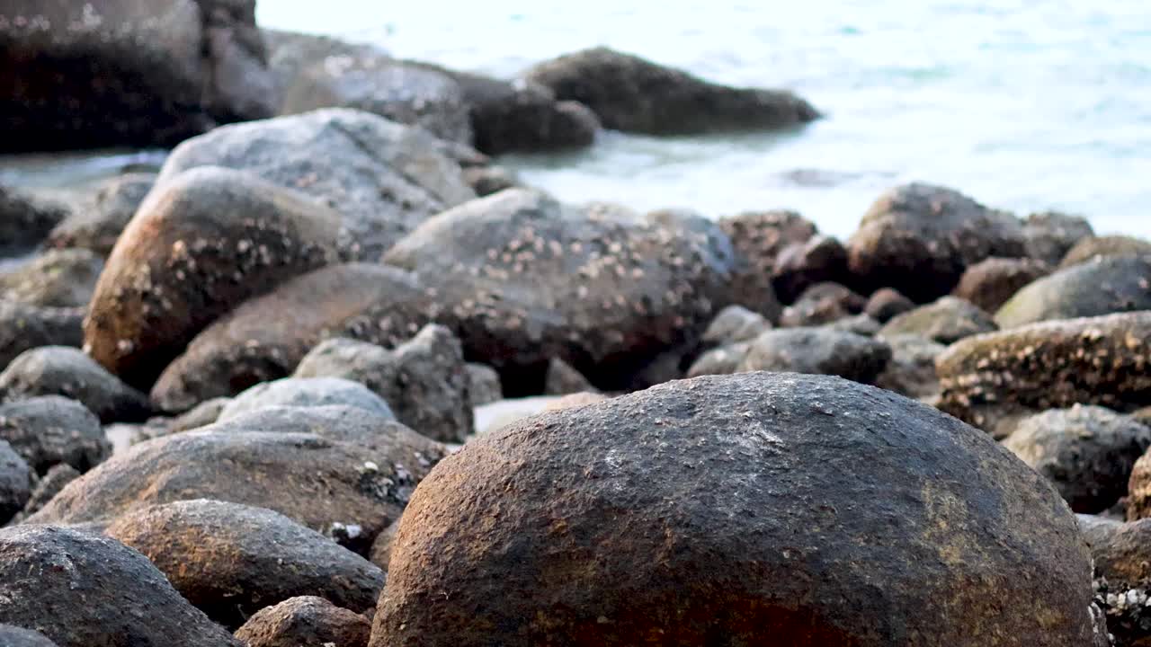 Waves gently lap against barnacle-covered rocks on a serene Phuket beach, captured in natural daylight