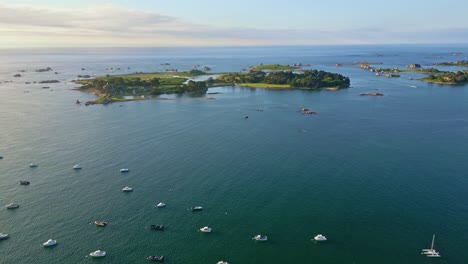 drone flies high above the sea at port-blanc, showing moored boats, distant islands, and a sunset sky. bretagne, france