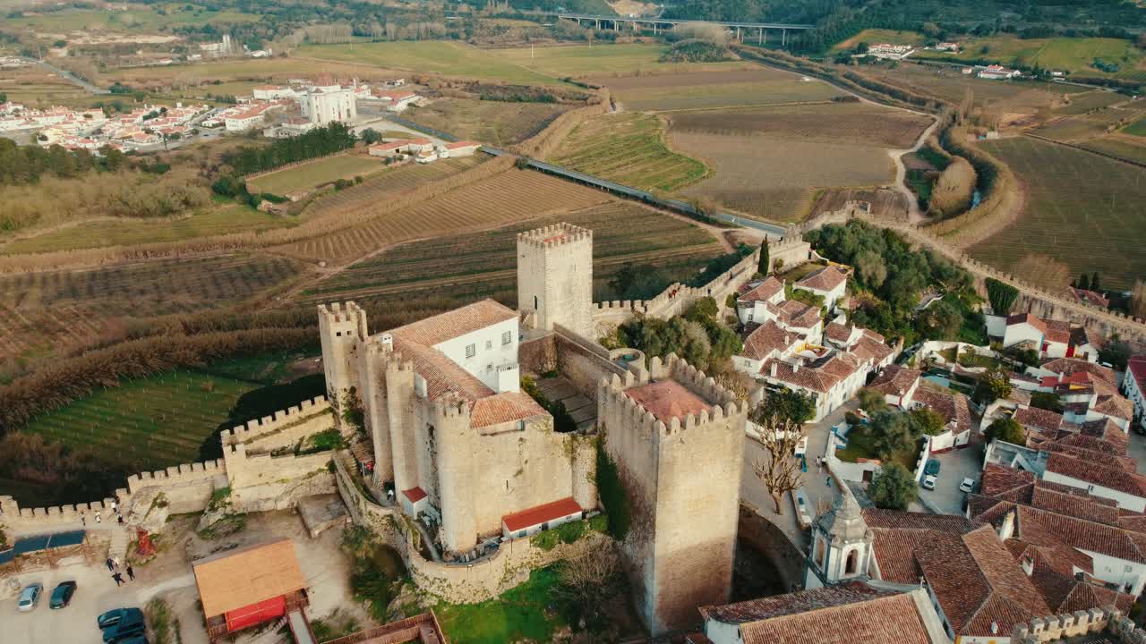 Ripresa cinematografica aerea con drone della Torre Dom Fernando a Óbidos, partendo da una vista elevata e arretrando lentamente per rivelare meglio la città medievale e il paesaggio circostante