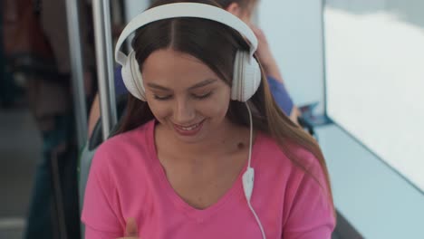 young woman passenger enjoying trip at the public transport, sitting with headphones near the window in the modern tram.