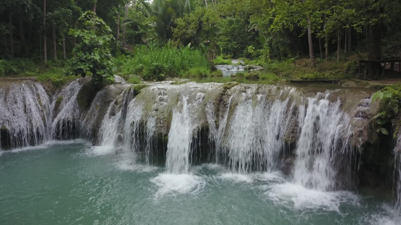 Ripresa con drone che avanza verso una cascata tropicale e una piscina naturale circondata da una giungla lussureggiante a Siquijor, Filippine