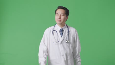 asian male doctor with stethoscope looking around and walking on green screen background in the hospital