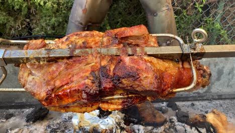 roasting suckling pig on a spit metal rotating stick over fire, extra crispy skin, pork bbq grill, 4k static shot