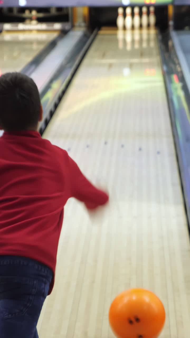 Young boy in red shirt is preparing to bowl at a vibrant bowling alley, with colorful lights and pins in the background, showcasing a fun recreational activity