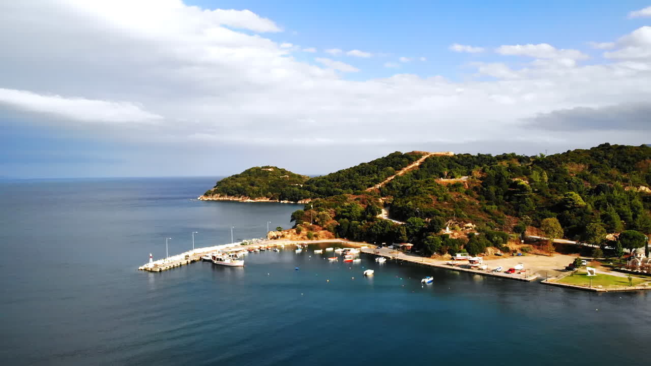 View of harbour with moored boats in Olympiada, Greece. Calm water of Aegean sea. Hills covered with greenery