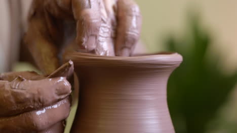 close up skilled potter moulding wet clay turning on workshop pottery wheel