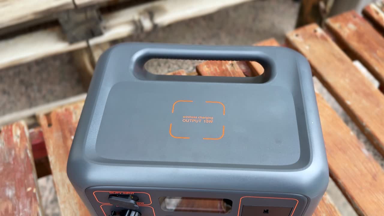 Primo piano di una stazione di alimentazione portatile con ricarica wireless su una panchina di legno all'aperto alla luce del giorno, che evidenzia un'attrezzatura energetica di riserva compatta e un moderno design di ricarica portatile.