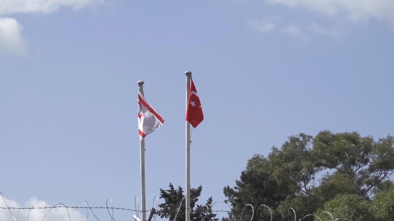 Flags of Turkish Northern Cyprus and Turkey waving in wind behind barbed steel fencing wire