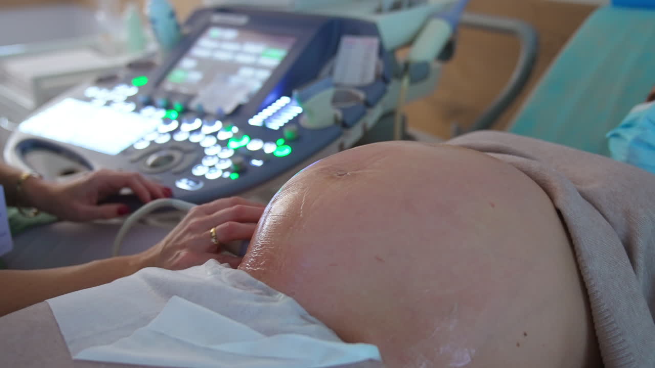 Big abdomen covered with gel of a pregnant lady. Doctor does the ultrasound examination to a future mom at last months of pregnancy.