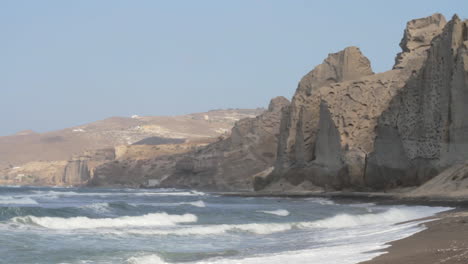 un hombre camina solo en una playa de arena negra rodeada de formaciones de acantilados volcánicos blancos en la isla de santorini, grecia