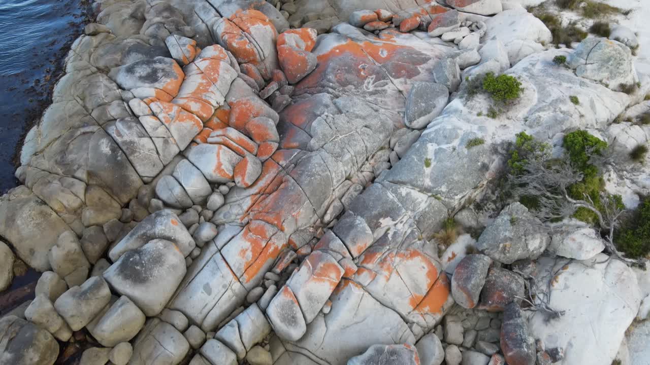 Drone liikkuu hitaasti eteenpäin ilmasta ja panoroi ylöspäin punaisten Bay of Fires -kallioiden ja aaltoilevan sinisen valtameren yli.