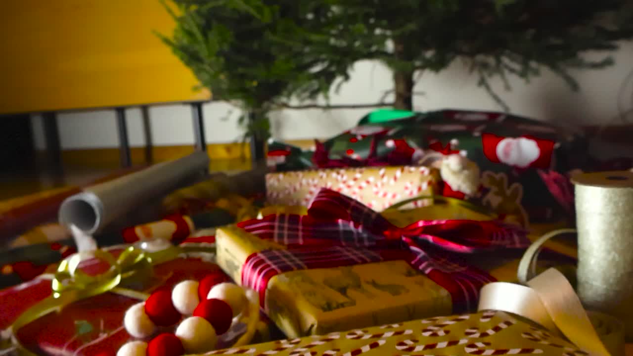 la cámara se levanta lentamente para revelar regalos de vacaciones de navidad y regalos en magnífico papel de envolver y cintas rojas bajo un árbol de navidad en el interior.