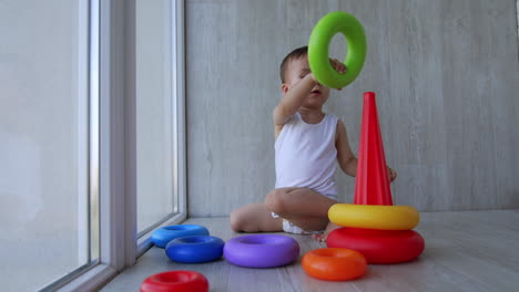 adorable caucasian baby boy plays at balcony. first kid looks into window and then collects pyramid.