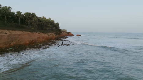 wide aerial footage off the coast of the gambia in the morning showing a man on a rock fishing in the waves