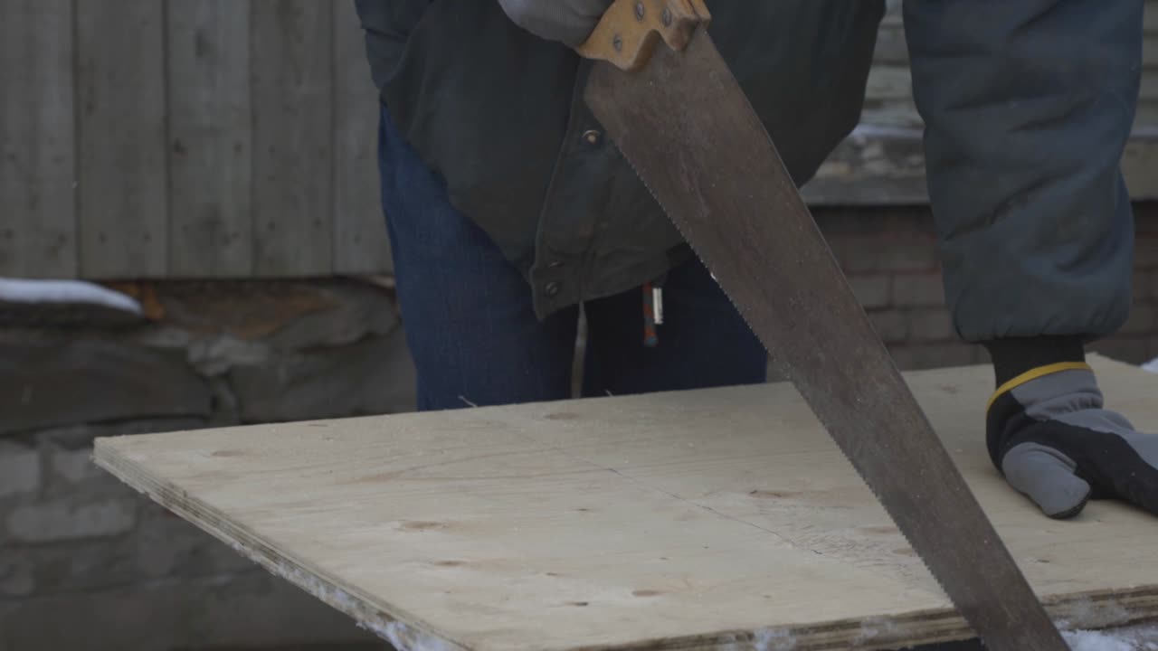 Un lavoratore che tiene in mano la sega a mano e inizia a tagliare il legno duro.