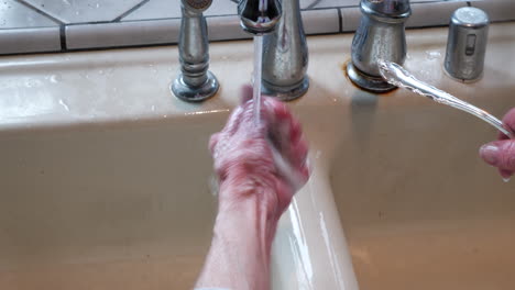 The-wrinkled-hands-of-an-old-woman-polishing-and-rinsing-a-piece-of-silverware-in-the-sink-to-remove-tarnish-and-make-it-shiny