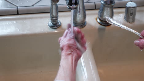 the wrinkled hands of an old woman polishing and rinsing a piece of silverware in the sink to remove tarnish and make it shiny