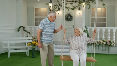 Senior-couple-together-in-front-yard-at-home.-Man-swinging-woman.-Happy-elderly-pensioners-family