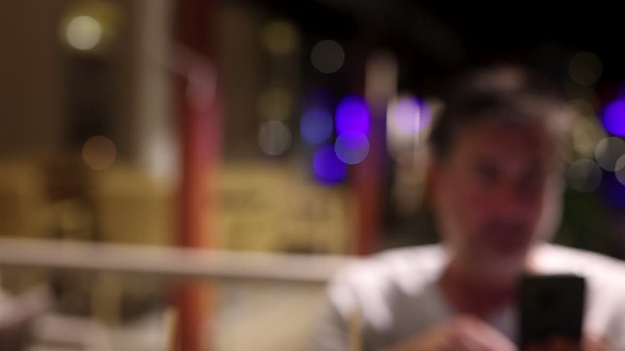 A man in a restaurant uses his phone, captured in a series of blurred frames with ambient lighting