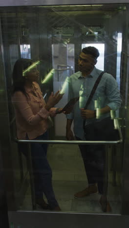 video vertical de felices y diversas trabajadoras y compañeros de trabajo hablando en el ascensor