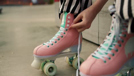 close-up: a character in striped pants sits on a bench and laces up his pink skates. preparing for roller skating in the skate park in summer