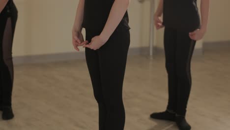 un grupo de jóvenes estudiantes de ballet con ropa de baile negra practicando posiciones en un amplio estudio de ballet con pisos de madera y barras montadas en la pared. expresiones enfocadas y movimientos sincronizados.
