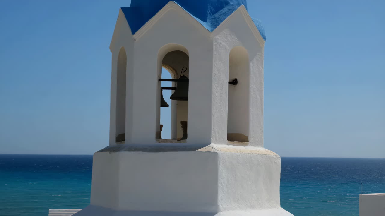 Iconic white bell tower with blue dome against a clear sky and sea