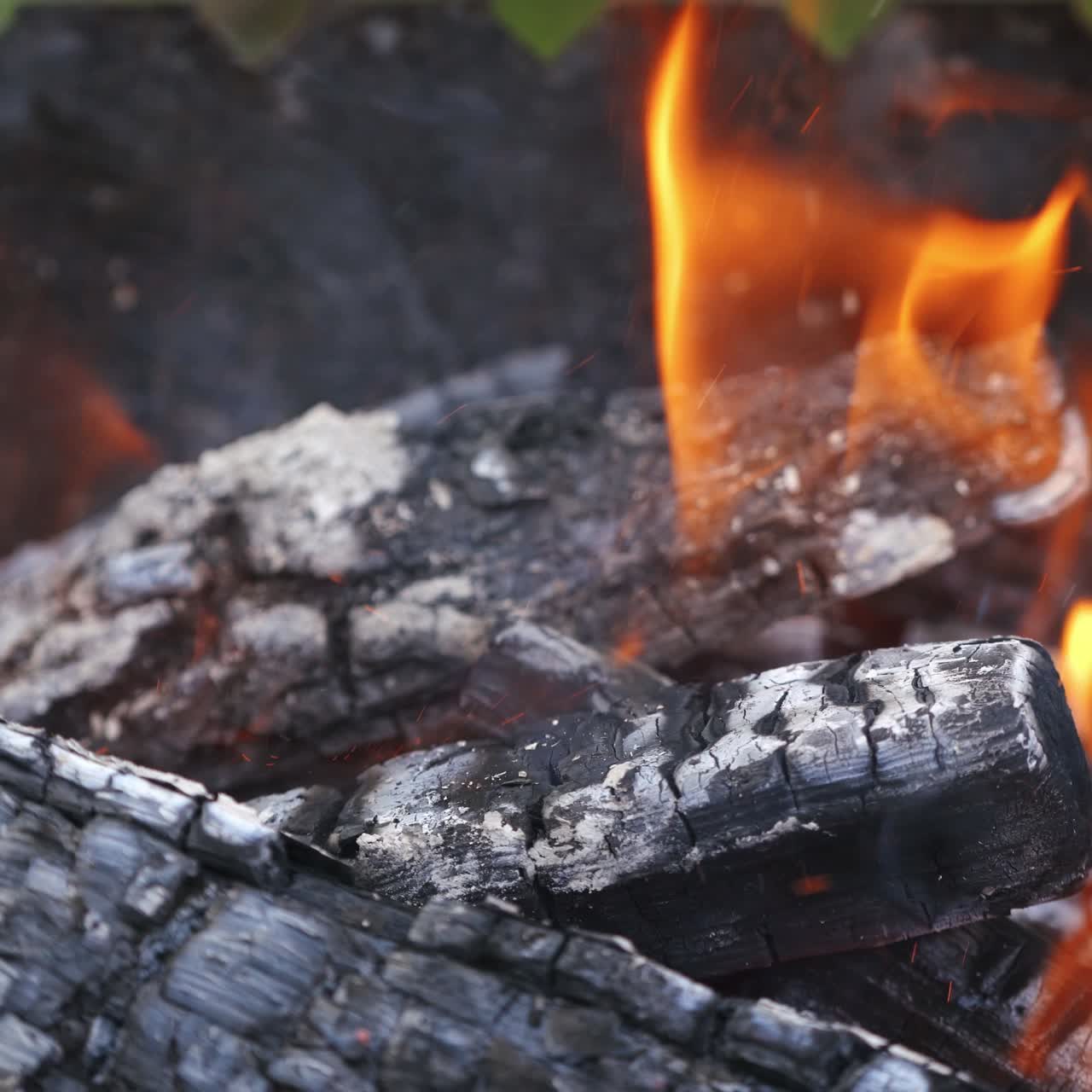 Smoldering charcoals in grill. Wooden stick turning over smoldered logs in fire. Burning wood in fire. Sparks in fire over smoldered logs. Close-up.