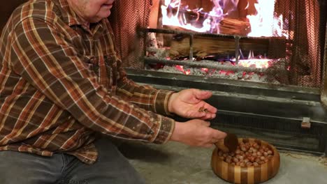 el anciano está usando una galleta de nueces hecha a mano para abrir avellanas mientras se sienta en la chimenea