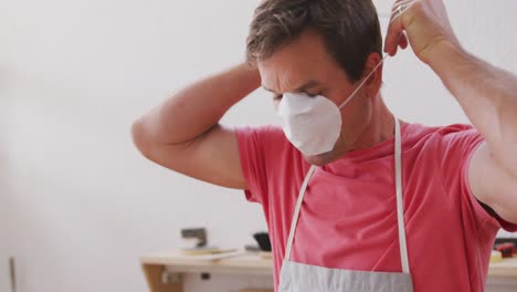 caucasian male surfboard maker wearing a protective apron and putting on a face mask