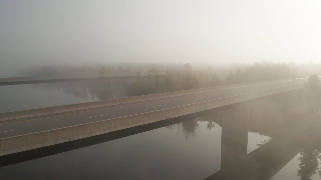 아침 안개가 고속도로 다리 위에 매달려 있으며, 안개를 통해 빛나는 빛으로 평온한 강을 건너고 있습니다.