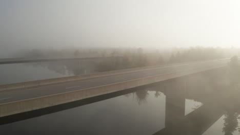 Morgennebel-Hängt-über-Der-Autobahnbrücke,-Die-Einen-Ruhigen-Fluss-überquert,-Und-Das-Sonnenlicht-Scheint-Durch-Den-Nebel