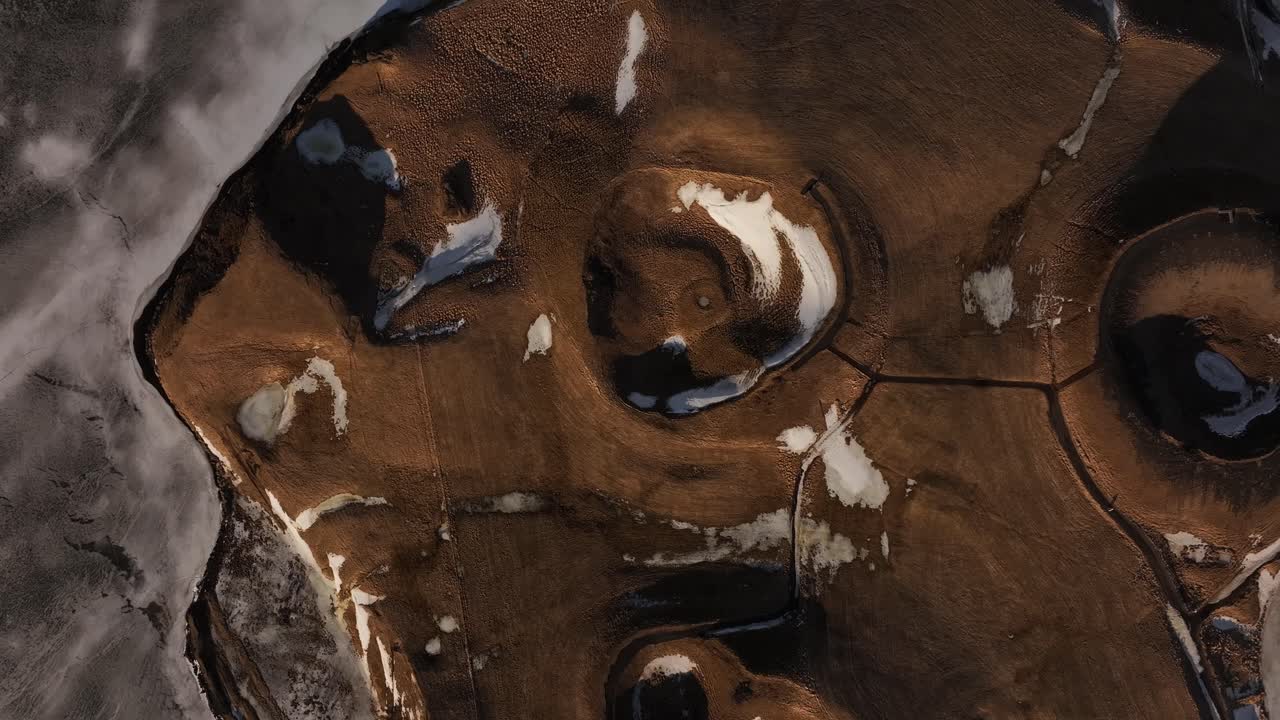 Top-down view of the volcanic pseudocraters near Lake Mývatn in Skútustaðir, Iceland, partially covered with snow and surrounded by icy terrain.