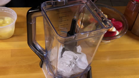 putting ice cubes and mixed fruit along with pineapple juice into blender for fruit smoothie