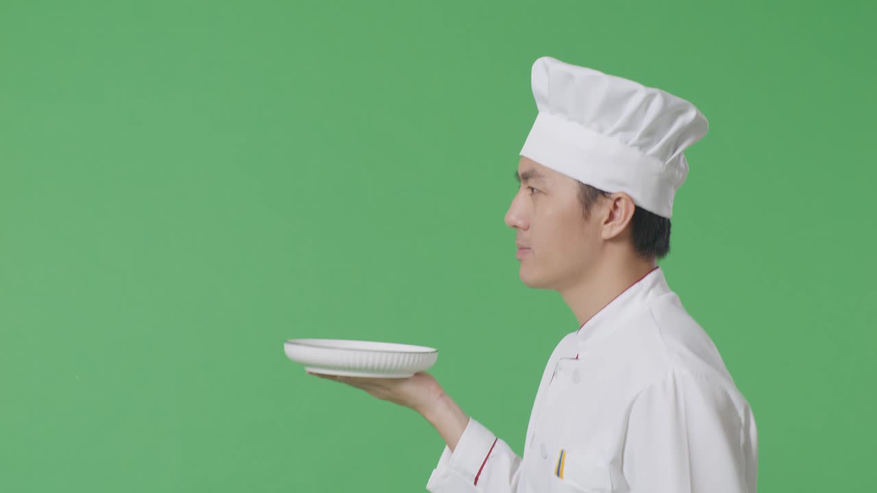 녹색 스크린 배경 스튜디오에서 는 동안 접시를 들고 있는 아시아 남자 셰프의 측면 시각