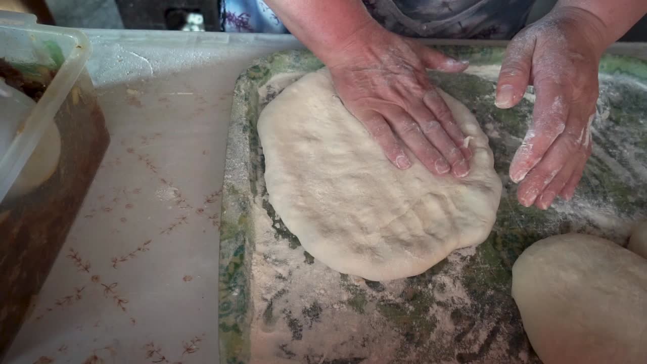 mujer manos desnudas haciendo masa para un pan georgiano plano en una tabla de plástico con harina, tiro superior