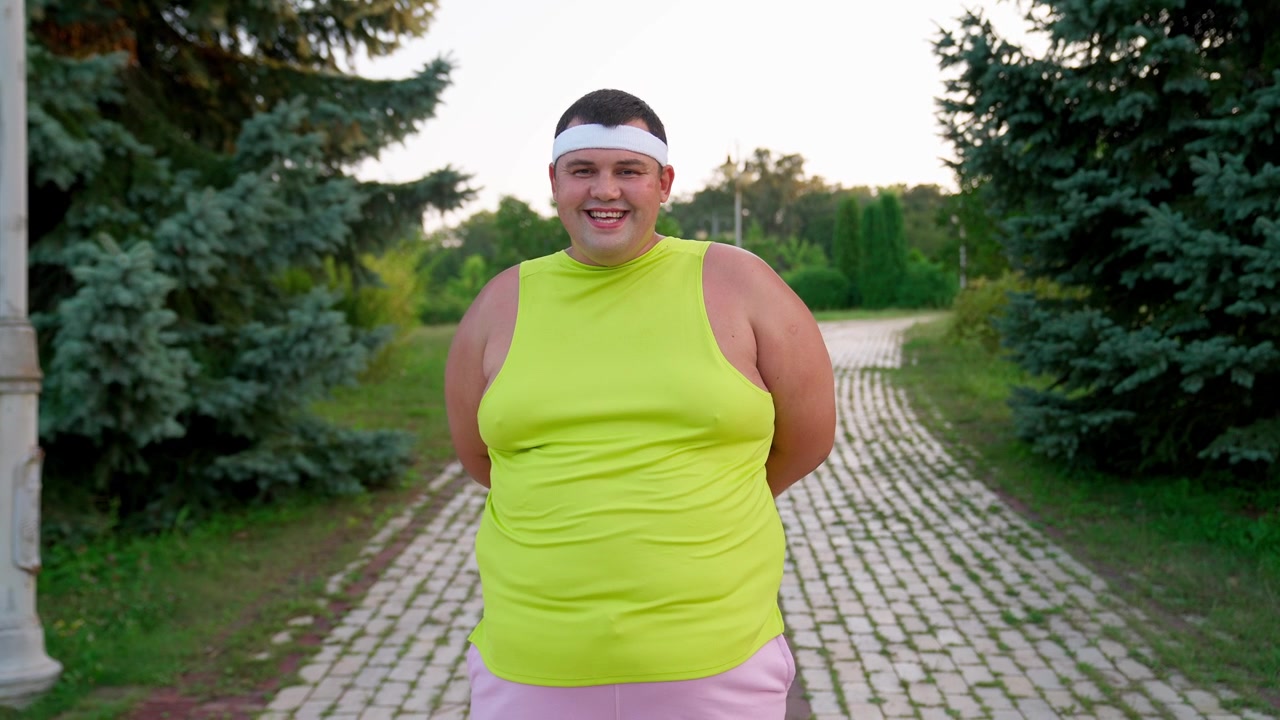 Uomo felice in sovrappeso in abbigliamento sportivo che sorride in un parco
