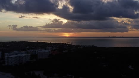 Beautiful-Aerial-drone-time-lapse-shot-of-a-stunning-orange-golden-ocean-sunset-with-tropical-greenery-below-from-Crandon-Park-in-Key-Biscayne-outside-of-Miami,-Florida-on-a-warm-sunny-summer-evening