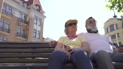 grandparents in modern clothes and accessories relaxing on bench in the city