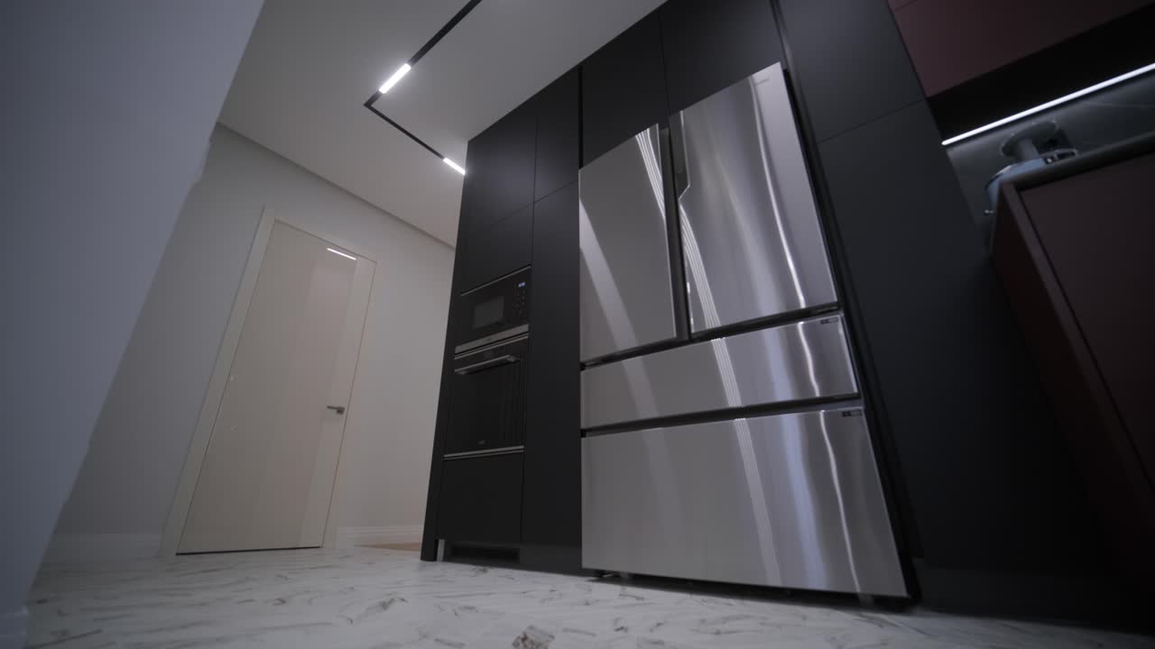 una cocina moderna con elegantes gabinetes negros, electrodomésticos de acero inoxidable e iluminación integrada en una habitación con suelo de mármol