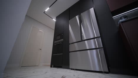 a modern kitchen with sleek black cabinetry, stainless steel appliances, and integrated lighting in a marble floored room