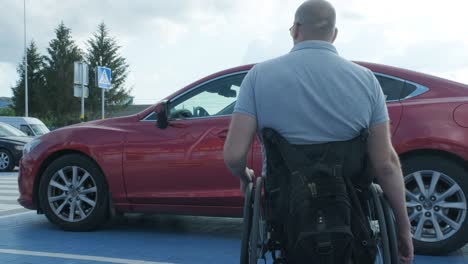young handicapped driver getting in red car from wheelchair