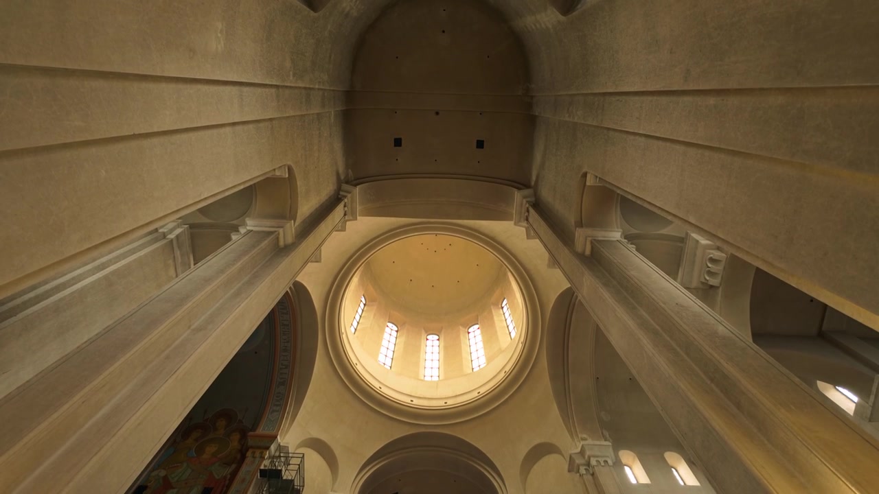 Grand interior view of the Holy Trinity Cathedral in Tbilisi, Georgia, looking up at its towering dome and massive supporting pillars. Displays intricate architectural design and scale.